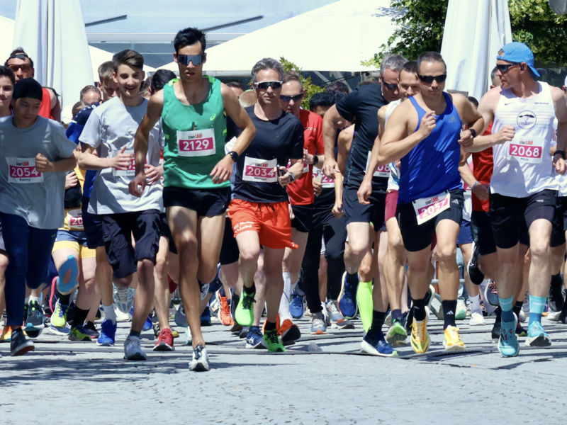 Große Gruppe von Läufern beim Stadtlauf in vollem Lauf kurz nach dem Start
