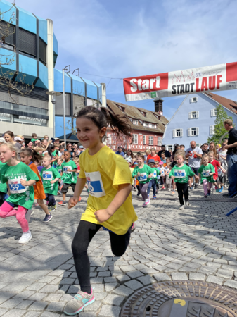 Gruppe von Kindern in grünen Trikots in vollem Lauf beim Waiblinger Stadtlauf. Im Vordergrund ein Kind in gelbem Trikot